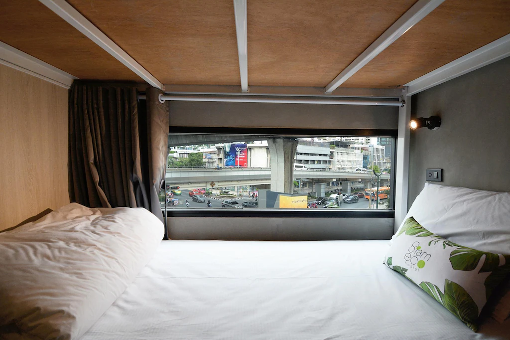 A capsule bed at Siam Eco Hostel with the Bangkok Skytrain visible through the window