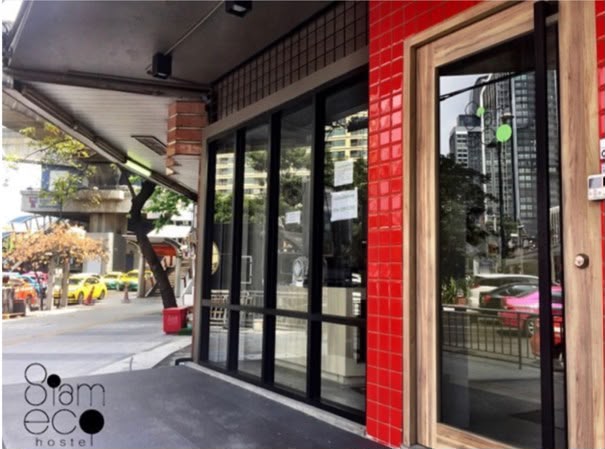 The red-tiled entrance of Siam Eco Hostel from street level, with the BTS Skytrain visible